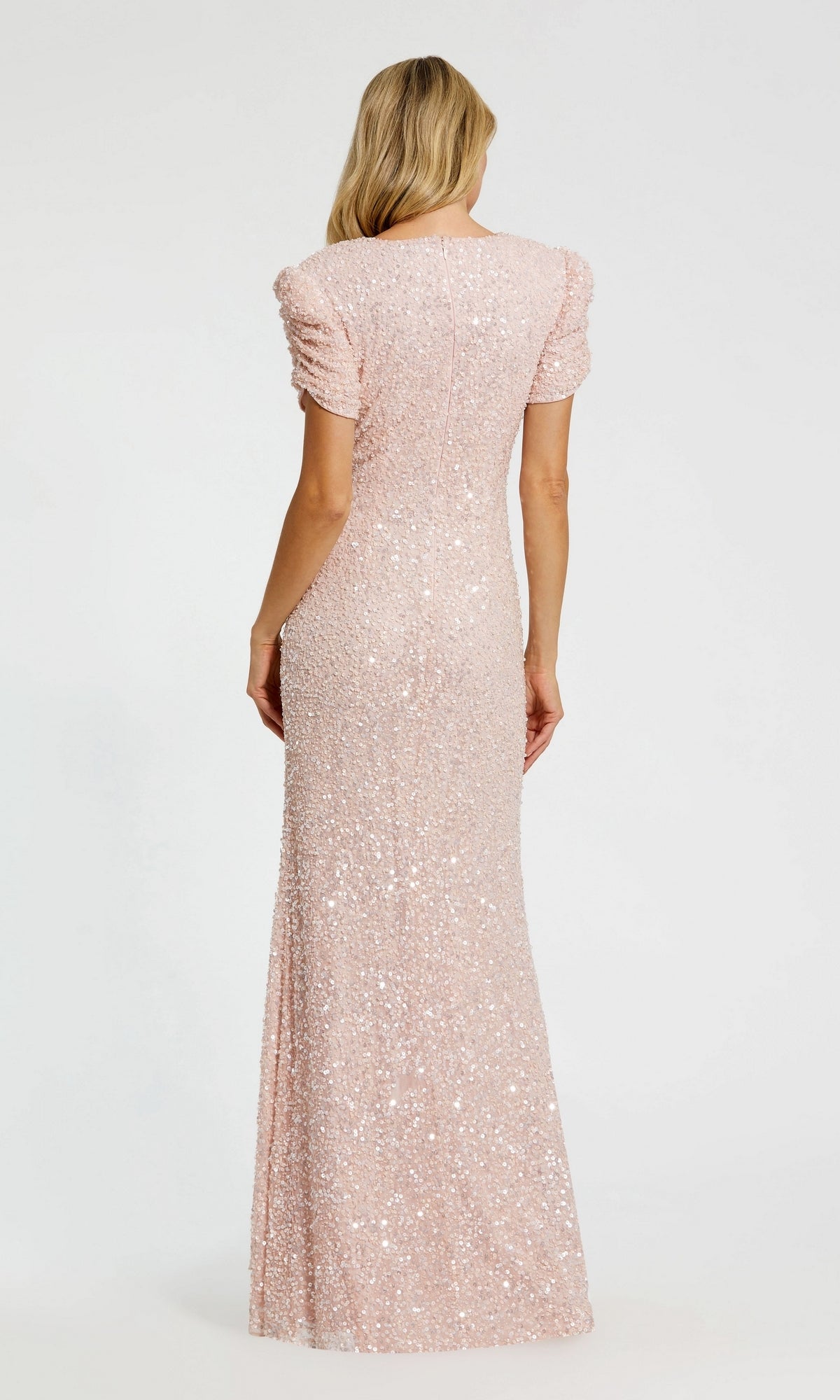 A blonde woman, seen from the back against a plain light background, wears the Mac Duggal 24003 Short Sleeve Sequin Formal Dress in light pink, a floor-length formal gown.